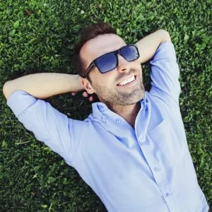 A man reclining on grass, enjoying the benefits of prepless veneers.