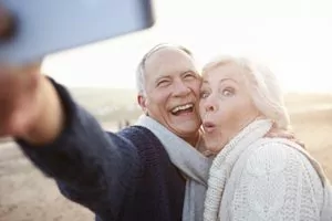 A mature couple smiling outside while taking a selfie, confident from new dentures.