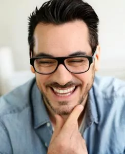 A young man wearing glasses, smiling proudly with healthy teeth.